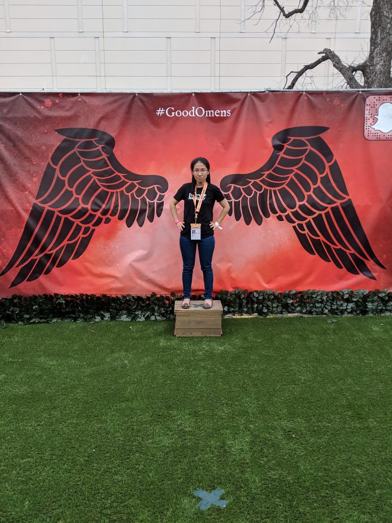 Founder/Editor of Geek Gals ChinLin Pan poses in front of a canvas of black angel wings.