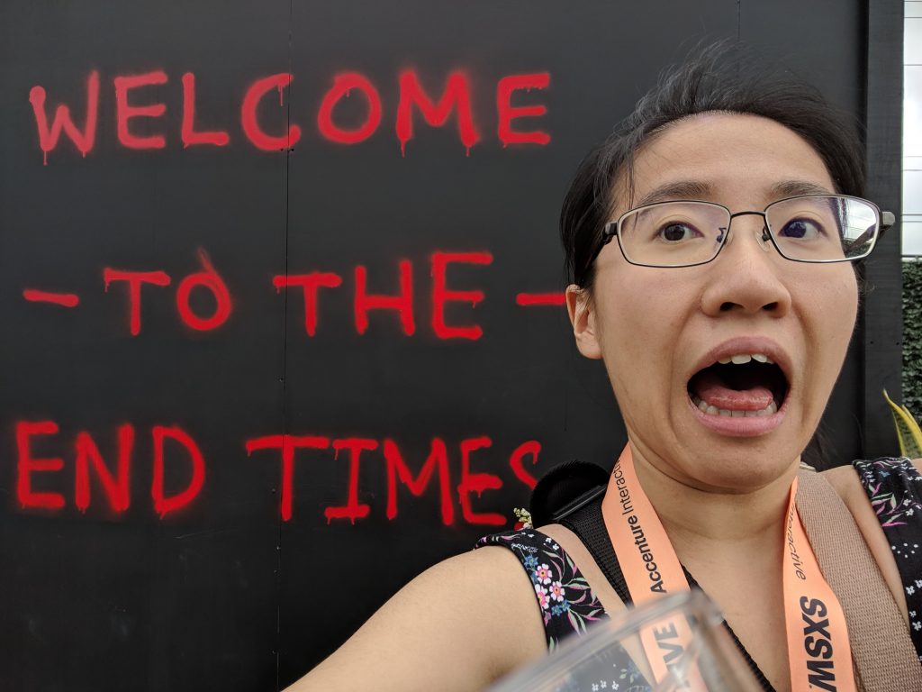 Founder/Editor ChinLin in front of a black wall with writing in red: Welcome To The End Times