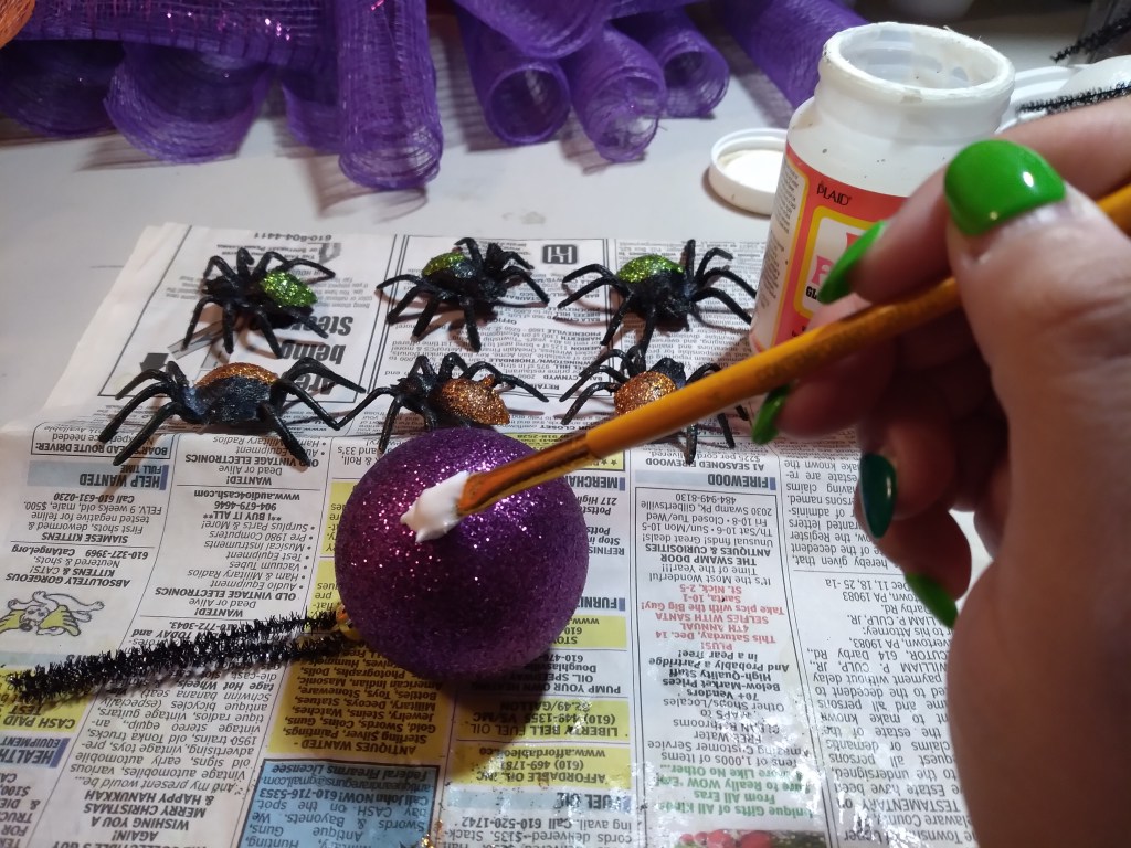 Melissa Joy applies glue to a purple, glittery ball that will be part of her Halloween wreath.