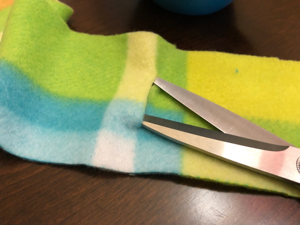 Close-up of scissors cutting a small slit in the DIY fleece koozie
