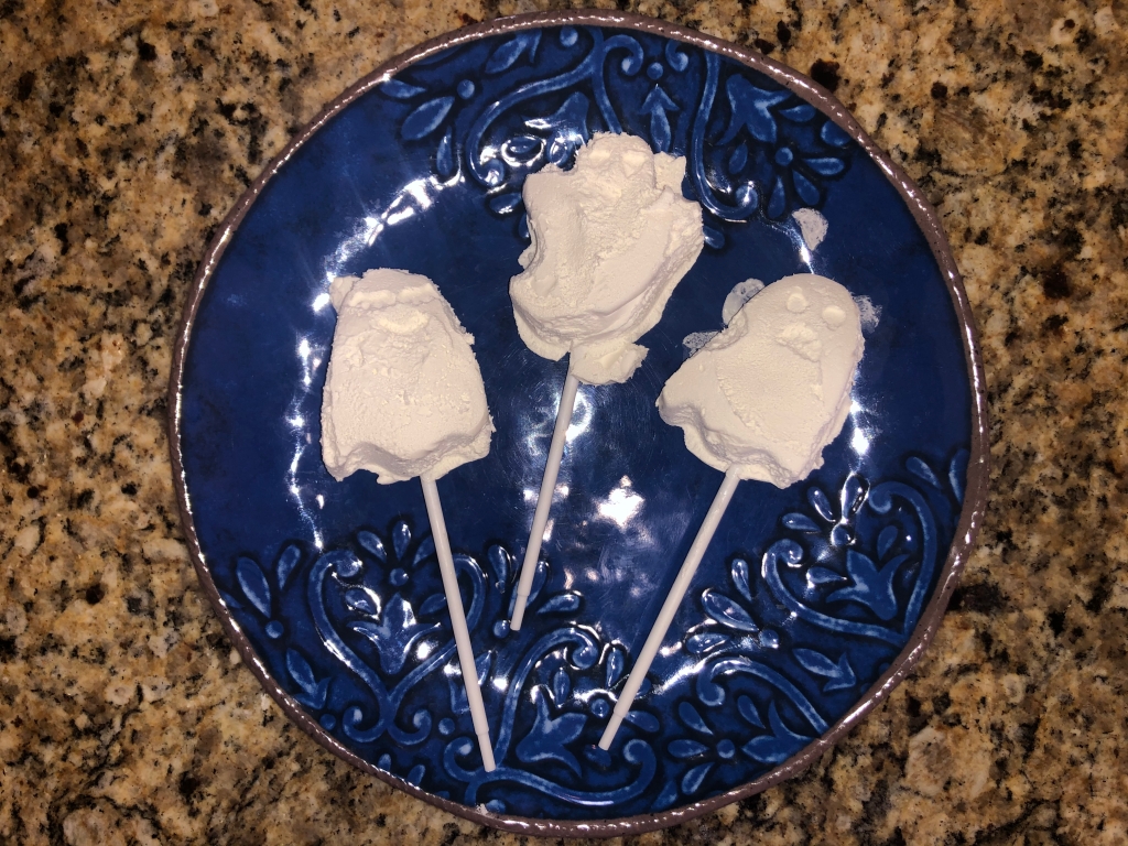 Three frozen Cool Whip ghosts on sticks on a navy blue ceramic plate