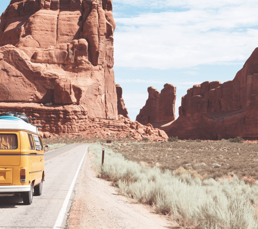 A yellow Volkswagon driving into a canyon, its inhabitants on a road trip.