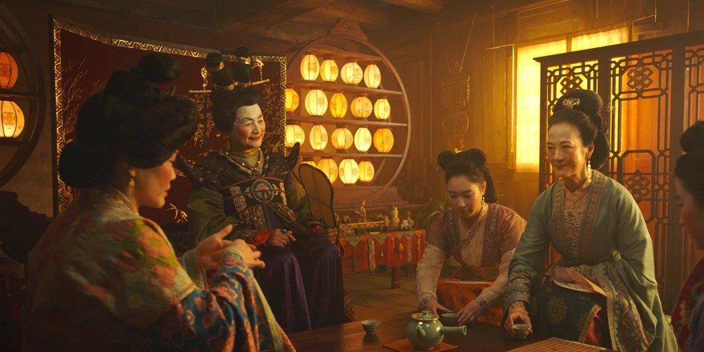 The town Matchmaker tries to teach Mulan how to serve tea properly as her sister and mother (right) sit beside her in Disney's live-action "Mulan"