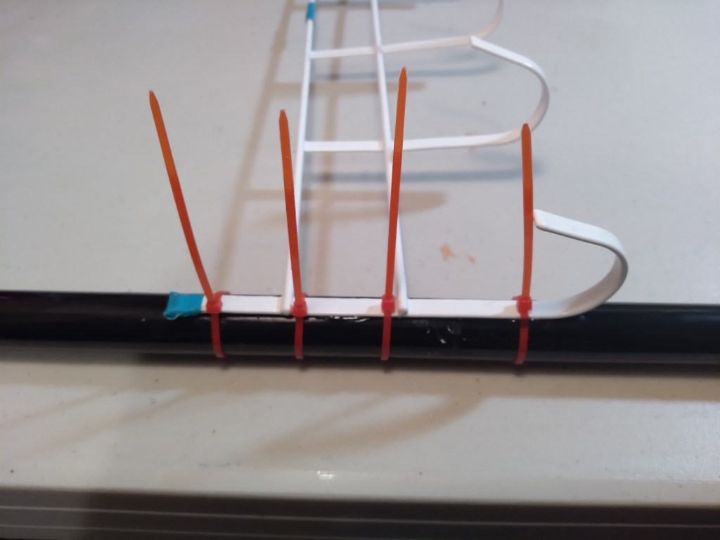 Use zip-ties to secure the broom pole and door hanger in between the bars.