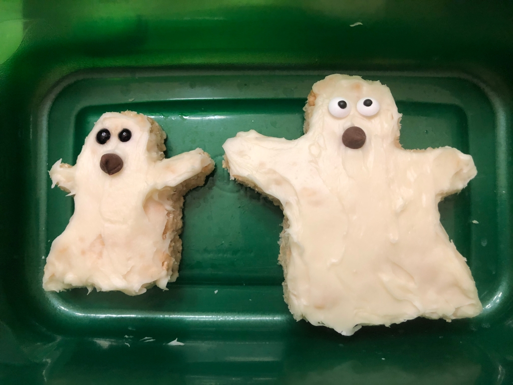 Two ghost-shaped Rice Krispy treats with white icing and decorations for the eyes and mouth 