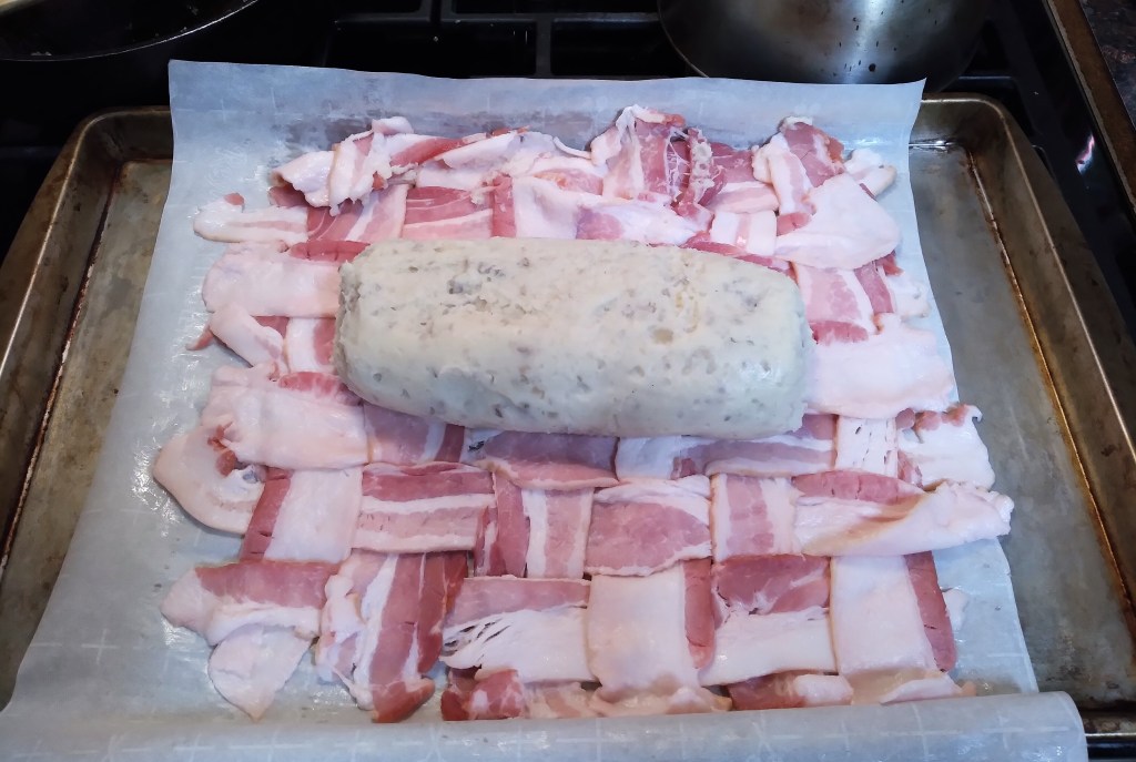 A potato shaped like a log on top of the bacon weave, ready to be wrapped